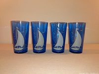 Front view of four cobalt blue Hazel-Atlas drinking glasses with white sailboat design, showing shape and decoration.