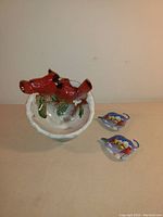 Front view of the decorative winter ceramic bowl with red cardinal bird perched on snowy greenery. Two small cardinal teabag holders placed next to the bowl.