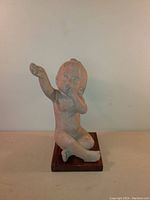Front view of the baby reaching up stone sculpture on wood base.