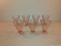 Photo shows a set of seven pink Depression era parfait glasses arranged in two rows, displaying their beveled sides and circular bases.