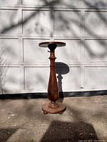 Full view of vintage round oak pedestal table showing height and design against a garage door backdrop in outdoor lighting.