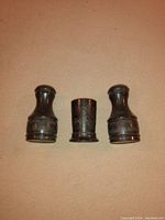 Three antique sterling silver pieces: two shakers and a toothpick holder with engraved floral and gourd designs, placed upright on surface.