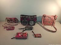 Four Vera Bradley bag sets displayed with matching wristlets and coin wallets against a plain background. Shows front view and arrangement of each bag with accessories.