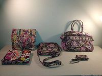 Photo with the whole set displayed, showing tote bag, duffel bag, satchel, wristlet, and scarf arranged on a flat surface against a plain background.