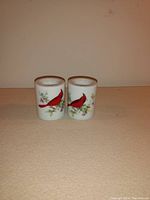 Front view of two ceramic candleholders showing the cardinal bird design on the outside.