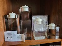 Four clear crystal candle holders displayed on wooden shelf, one holder lit with a white candle, original Rosenthal box visible behind one holder.