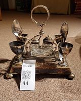 Full view of boiled egg stand with six egg cups on a square tray, central glass condiment dishes, and spoons.