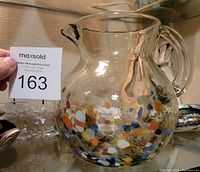 Front angled view of clear glass pitcher with multicolored confetti dots and handle, showing size with auction card.