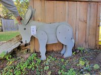 Full side view of the assembled wooden donkey sculpture standing outdoors against a wooden fence with dimensions tag visible.