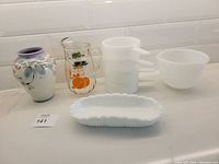 Lot overview showing ceramic vase, clear glass orange pitcher, stack of four milk glass soup bowls, opaque glassbake mixing bowl, and milk glass trinket dish