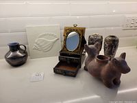 The lot displayed on a white countertop includes the terracotta two-headed dog planter, Chinese jewelry box with mirror and drawers, blue glazed pitcher, two Japanese Satsuma Moriage vases with intricate decoration, and the white 3D shell relief panel.