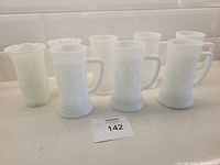 All six white milk glass beer steins and two milk glass vases shown on a white surface.