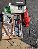 Top down photo showing grouped tools on cardboard box including red floor jack, mixing paddle, caulking gun, white tray with miscellaneous tools, dustpan and brush