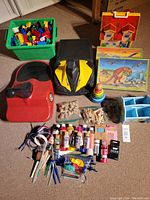 Photo showing entire lot including Zipfy sleds, Lego blocks in green bin, wooden craft boxes, puzzles, paints, and craft supplies.