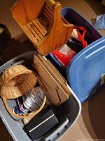 Wooden basket with stains, two plastic bins (blue with lid, gray without lid), cardboard mailers, wicker basket, and other storage items inside bins.