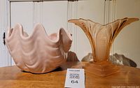 Photo of both the pink ceramic clam shell vase and amber Art Deco depression glass vase together on a wooden surface against a white wall.