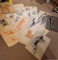 Overall spread of multiple nude sketches on carpeted floor showing variety of red chalk and charcoal drawings.
