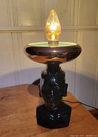 Front view of black ceramic bust lamp with gold bowl shade and vintage bulb lit