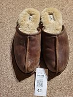 Top down view showing brown leather slippers with UGG label and natural scuff marks.