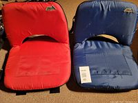 Front view of red and blue travel seat cushions showing cushioned seats, pockets, and brand logos