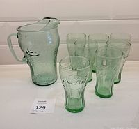 Full set of one green glass Coca-Cola pitcher and seven matching Coca-Cola tumblers arranged together for overview.
