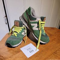 Pair of green New Balance running shoes shown on wooden surface, front and side angle. Yellow laces, white 'N' logo on sides, model style ML574ND visible on tongue tag.
