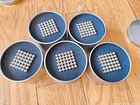 Five round metal cases each containing a cube of 216 silver magnetic balls arranged 6x6x6.
