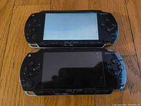 Front view of two Sony PSP 3000 handheld consoles, one with an active screen showing message and screen crack, other with screen off