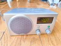 Front view of the Boston Acoustics Receptions AM/FM clock radio showing speaker, digital clock displaying 12:00, control knobs for tuning and volume, and power button.