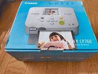 Image of the Canon Selphy CP760 compact photo printer depicted on the retail box, showing the printer and sample photo output.