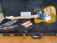 Full view of electric guitar in black hard case with strap and cable