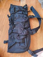 Front view of black gun bag showing three snap-button pockets and adjustable straps with buckles.