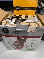 Photo of the front and top portion of the Keurig K10 Mini Plus retail box showing product image and branding, with some wear visible on the box edges