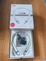 Top-down photo showing LG Tone Pro headset resting in plastic packaging alongside a sealed plastic bag containing charging cable, ear gels, and warranty card inside the original box.