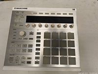 Top view of the Maschine MK2 controller showing pads, buttons, knobs, and LCD screen.