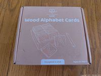 Closed pink box labeled 'Montessori Wood Alphabet Cards' with simple illustration and age recommendation.