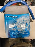 Front view of cooling unit showing Polar Care Kodiak blue and white plastic casing with ice graphics and Breg logo, hoses coiled on top.