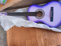Purple acoustic guitar unboxed showing the full body and neck with purple gradient finish.