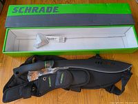 Green Schrade box with machete and nylon sheath laid out next to the box lid, showing machete's blade and handle.