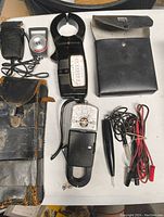 Top-down image showing all items including Weston clamp meter, analog meters, test leads, and leather cases on a table.