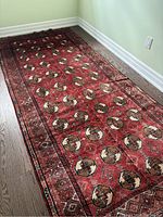 Full view of red Bokhara-pattern rug along hardwood floor and wall