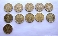 Top view of reverse (coat of arms) side of 11 Canadian 50 cent coins arranged in two rows.