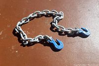 Photo of a 3-foot metal towing chain lying on a brown surface showing steel links and blue-coated grab hooks on each end.
