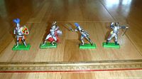 Front view of four vintage medieval knights in metal on green bases aligned alongside a ruler for scale.