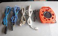 Photo of all extension cords and the orange extension cord reel laid out on a table, showing different colors and plug types.