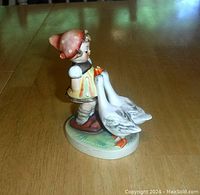 Side view of the porcelain figurine showing girl with headscarf and two geese, standing on oval base.