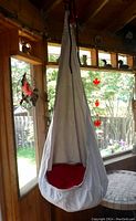 White fabric cocoon-style hanging chair suspended indoors with visible red cushion inside, viewed from a distance to show overall shape and hanging setup.
