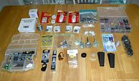 Top view of assorted hardware and household items spread on a table including knobs, screws, push pins, fishing tackle accessories packed in plastic containers and bags