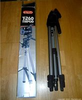 Original boxed OPTEX T-260 Tripod with tripod folded beside its box on a wooden surface.