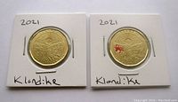 Obverse side of two 2021 Klondike Anniversary Loonies featuring the landscape design, with one coin plain and the other with a small coloured detail.